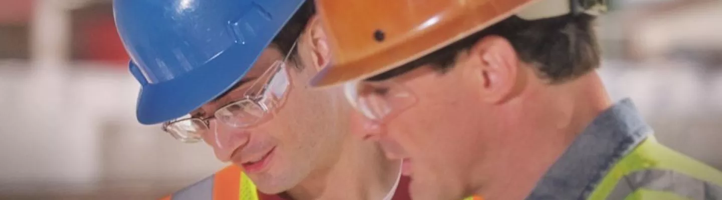 Two men on a construction site wearing hard hats, safety vests and safety glasses.