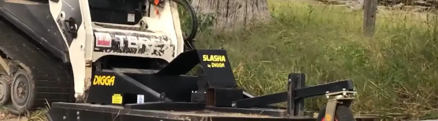 Slasher machine positioned in an open field, used for cutting grass or clearing vegetation near a worksite.