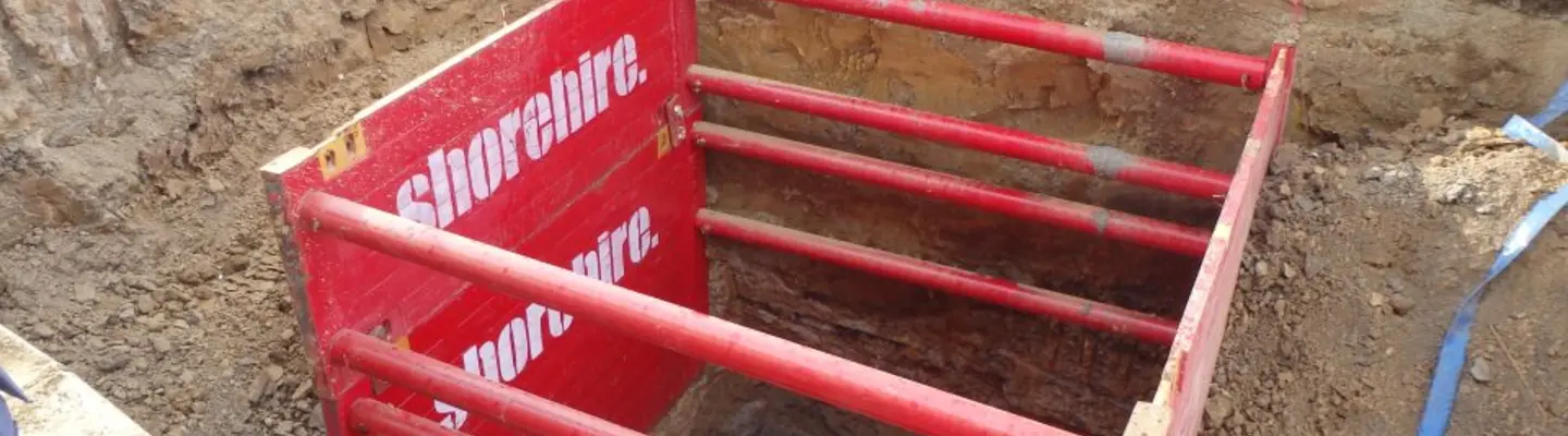 Workers installing internal props inside a shoring box placed in a trench to reinforce excavation walls and maintain safety.
