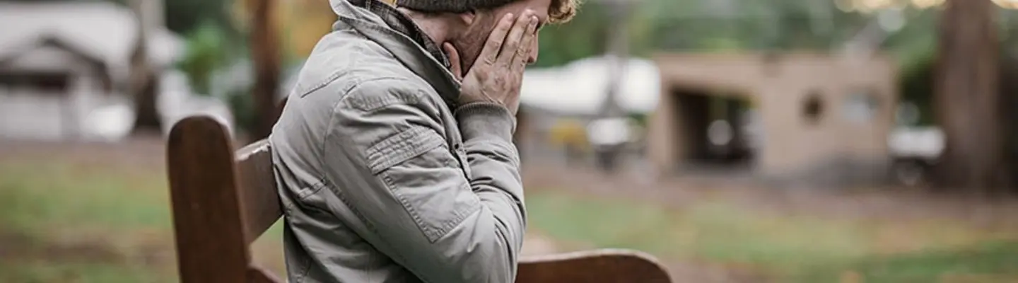 Sad man sitting alone on a park bench, appearing deep in thought during a quiet moment outdoors.