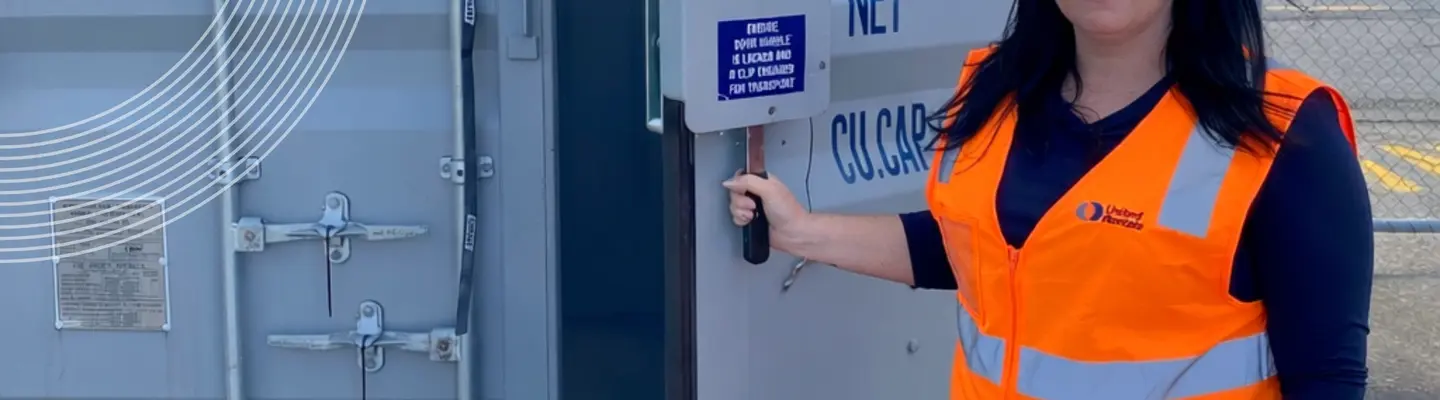 A woman in a hi-vis vest holding the door of a shipping container open.