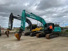 Man standing in a parked excavator at a construction site with safety barriers in the background.