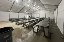 Rows of dark picnic tables arranged inside a spacious, brightly lit industrial tent, serving as a temporary breakroom.